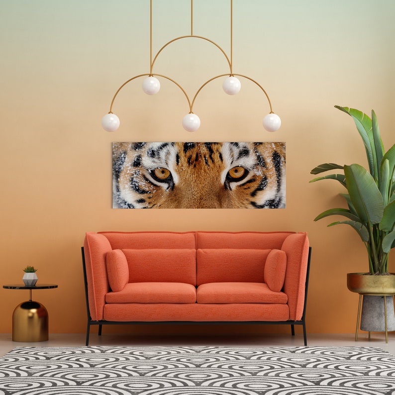 May include: A living room interior design with a modern orange couch, a black and white patterned rug, a gold side table, a potted plant, and a tiger's face artwork hanging on the wall.