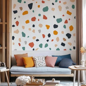 May include: A light gray couch with a variety of colorful throw pillows. The wall behind the couch is decorated with a terrazzo pattern in shades of orange, green, blue, and gray.