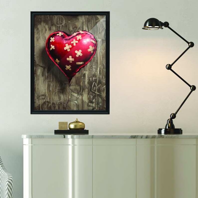 May include: A framed painting of a red heart-shaped balloon with multiple bandages on it. The balloon is floating against a brown and gray background with graffiti.