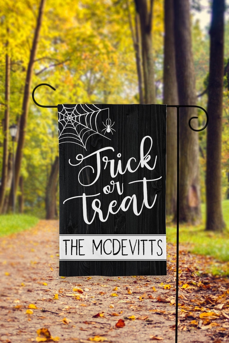May include: Black and white Halloween garden flag with a spider web and spider design. The text reads "Trick or Treat" with the name "The McDevitt's" below.