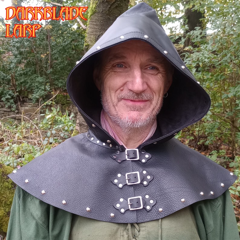 May include: A black leather hooded cowl with silver studs and buckles. The cowl has a pointed hood and a wide collar.