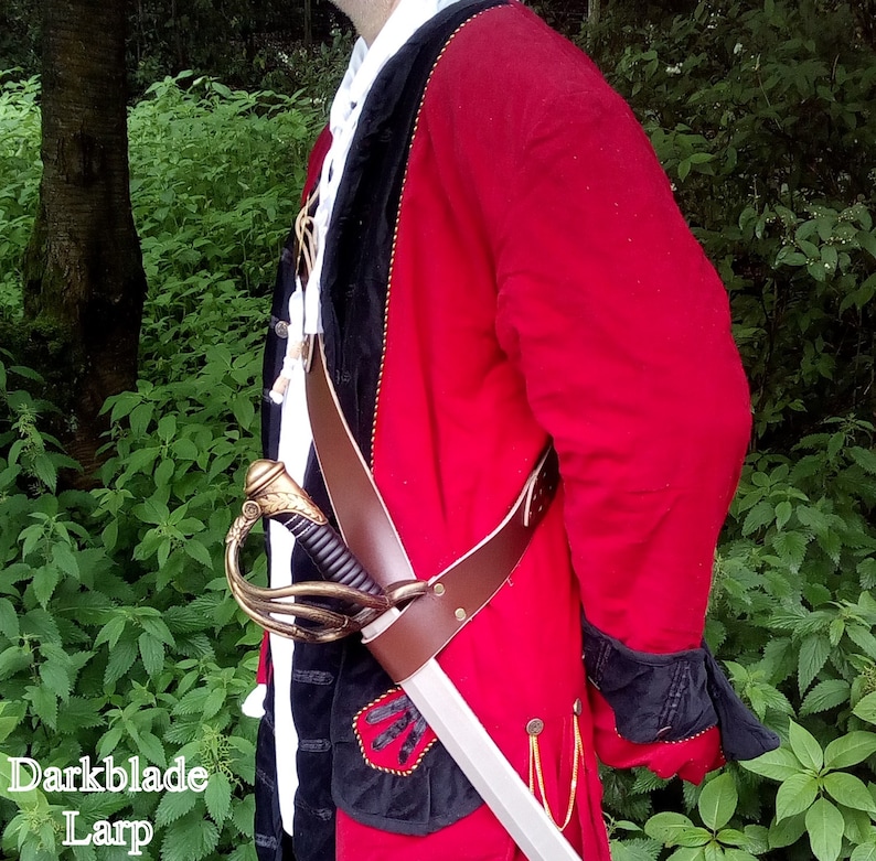 A Larp cutlass sheathed in a brown cross body abldric. The baldric is worn over a red and black frock coat and a white ruffled shirt.