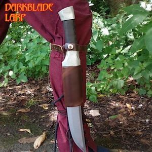 May include: A silver and black knife with a brown leather sheath is strapped to a red leg. The knife is secured with a brown leather strap and a metal buckle. The knife is worn on the outside of the leg.