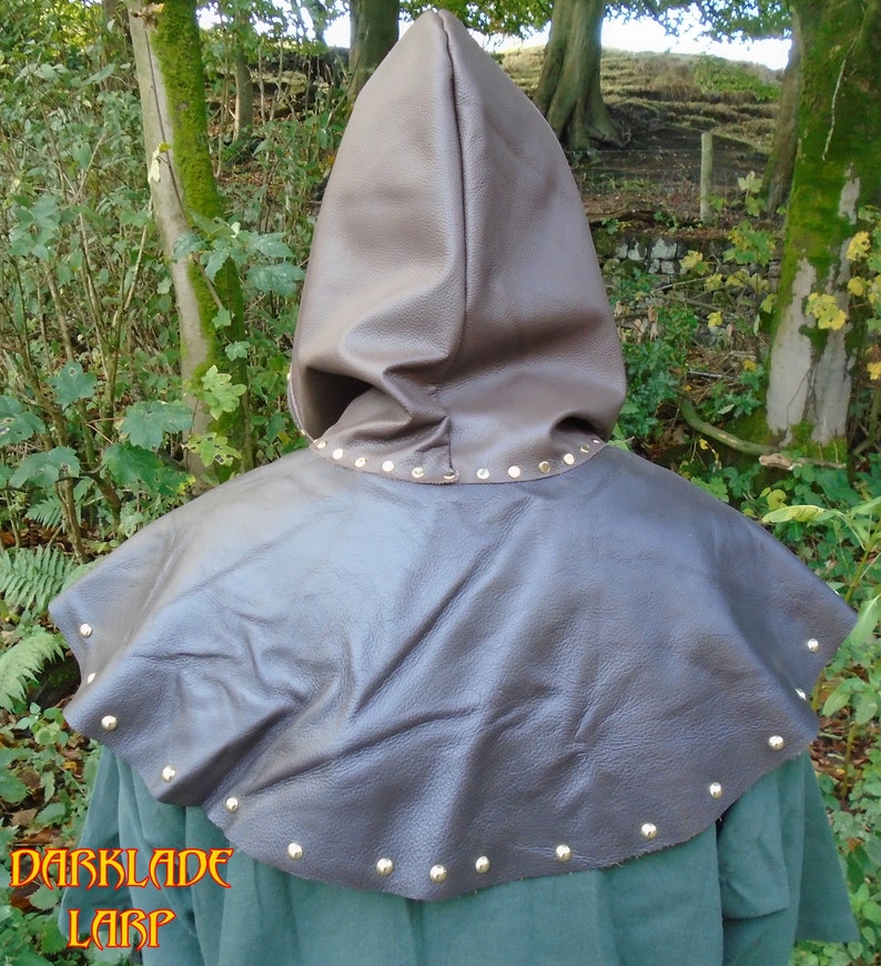 May include: Brown leather hooded cloak with a wide collar and metal studs around the edges. The hood is pulled up and the cloak is worn over a green shirt.