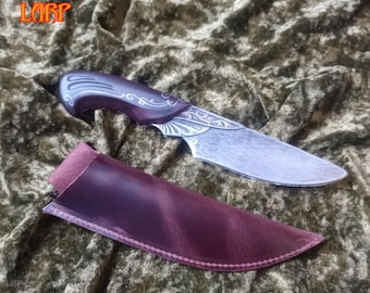 Puede incluir: Un cuchillo decorativo con una hoja plateada y un mango marrón oscuro con detalles plateados. Se presenta con una funda de cuero burdeos. El texto "DARKBLADE LARP" es visible en la esquina superior izquierda.