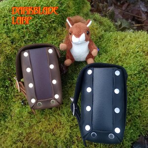 May include: Two leather pouches with metal rivets, one brown and one black, on a green mossy background.  DARKBLADE LARP is written in orange text on the top of the image.