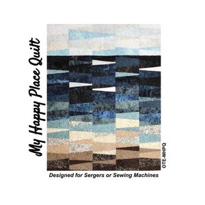 May include: A quilt with a layered design in shades of blue, black, tan, and white. The quilt features the text "My Happy Place Quilt" and "Designed for Sergers or Sewing Machines". The quilt has a geometric pattern.