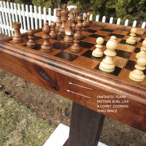 May include: A wooden chess set with dark and light brown squares and chess pieces. The board has a decorative edge and is supported by a dark wooden stand. The text on the side reads "FANTASTIC FLAME PATTERN BURL LIKE A COMET ZOOMING THRU SPACE."