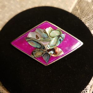 May include: A pink and silver brooch with a flower design made of iridescent abalone shell.