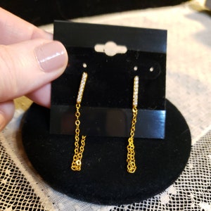 May include: Gold dangle earrings with a small bar of cubic zirconia stones and a delicate gold chain.