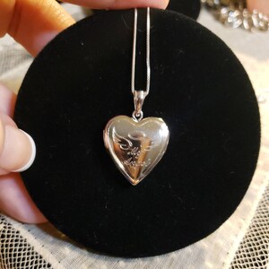 May include: Silver heart-shaped locket necklace with a delicate chain. The locket features an engraved angel with wings and the words "My Angel".