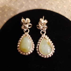 May include: A pair of silver dangle earrings with teardrop-shaped green stones set in a beaded border.