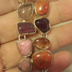 May include: A silver bracelet with a variety of colorful gemstones, including pink, red, orange, and purple. The bracelet is made of silver and has a polished finish.