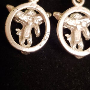 May include: A pair of silver earrings with a circular design featuring a stylized bird in the center. The earrings are marked with the number "925" on the back.