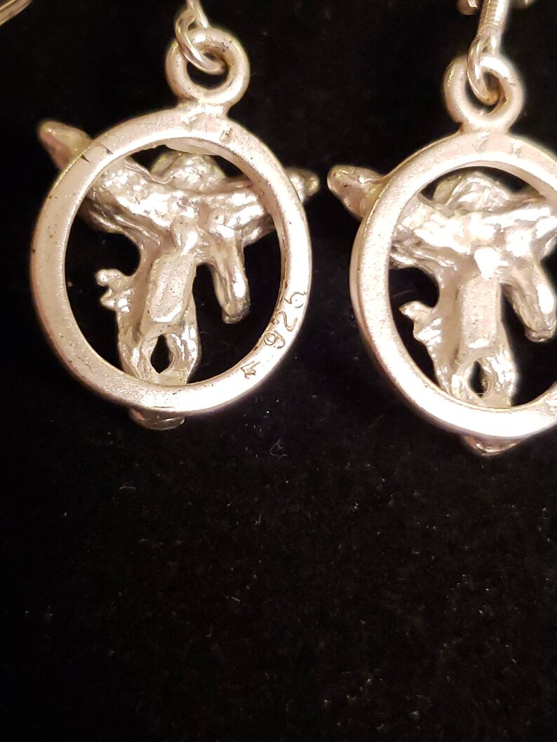 May include: A pair of silver earrings with a circular design featuring a stylized bird in the center. The earrings are marked with the number "925" on the back.