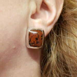 May include: A pair of silver square earrings with a red and black stone in the center.