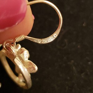 May include: Silver earring with a floral design and a hook closure. The earring is marked with the letters "925" on the hook.