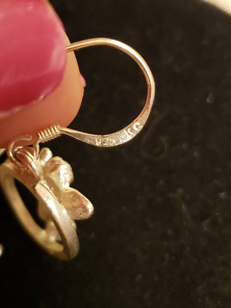 May include: Silver earring with a floral design and a hook closure. The earring is marked with the letters "925" on the hook.