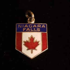 May include: A gold-colored charm with a blue and white enamel shield featuring the words "NIAGARA FALLS" and a red maple leaf.