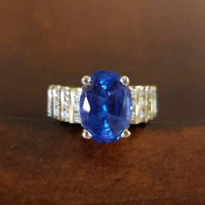 May include: A gold ring with a large oval blue sapphire gemstone surrounded by smaller diamonds.
