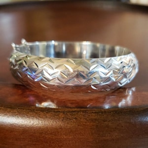 May include: A silver bangle bracelet with a textured diamond pattern.