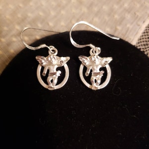 May include: A pair of silver earrings featuring a cherub design. Each earring has a small oval frame with a cherub figure inside.