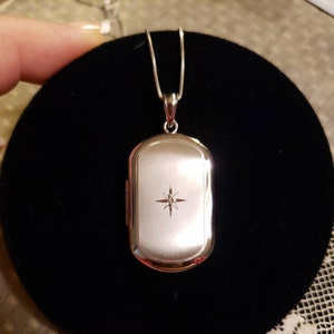 May include: A silver locket necklace with a diamond-shaped design in the center. The locket is rectangular and has a smooth, polished finish.