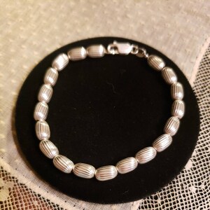 May include: A silver bracelet with a chain of oval-shaped beads. Each bead has a textured, ribbed design.