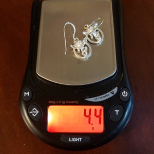 May include: A digital scale with a red display showing a weight of 4.4 grams. The scale is black with a silver top and a white button labeled "LIGHT".