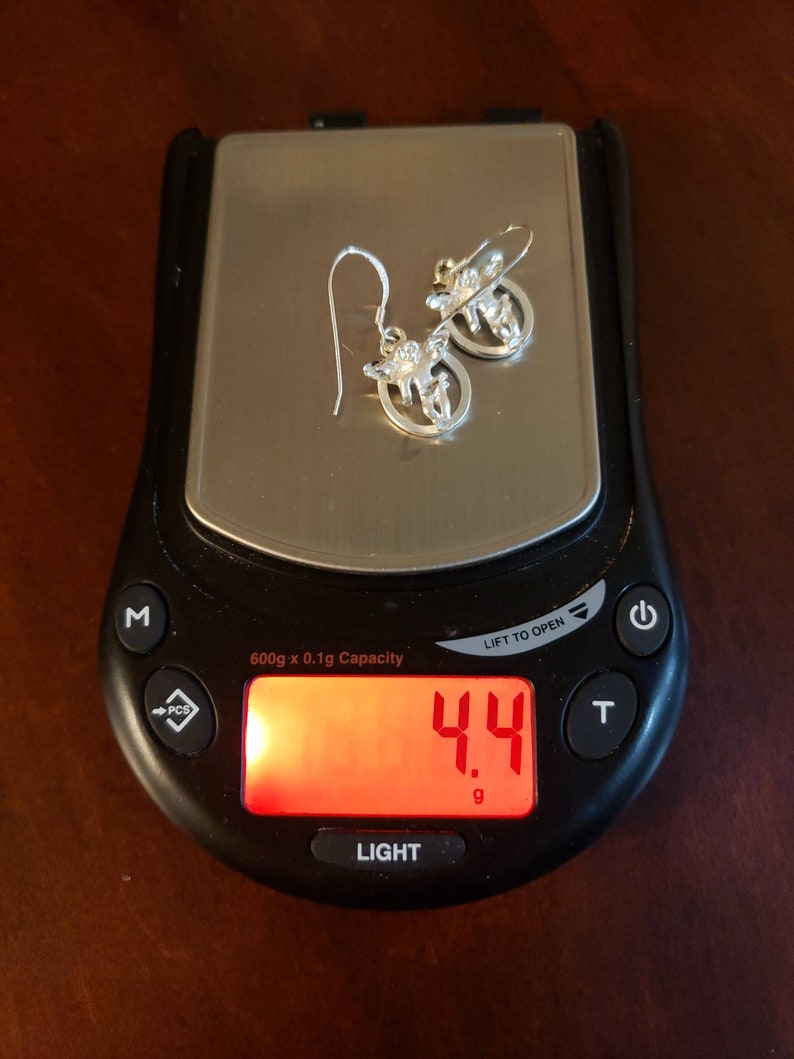 May include: A digital scale with a red display showing a weight of 4.4 grams. The scale is black with a silver top and a white button labeled "LIGHT".