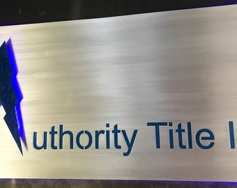 May include: A silver metal sign with a blue stylized "A" logo and the text "Authority Title Inc."