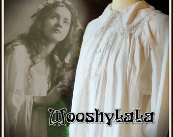 Op de afbeelding: Witte katoenen blouse met een kanten kraag en lange mouwen. De blouse heeft een gerimpelde look en wordt aan de voorkant dichtgeknoopt. De blouse is op een mannequin.