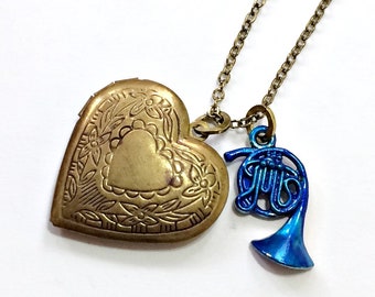 May include: A gold heart-shaped locket necklace with a blue french horn charm. The locket has an intricate floral design.