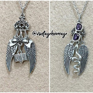May include: Silver necklace with multiple charms, including a pair of angel wings, a book, a bow, and a pair of glasses with purple stones.