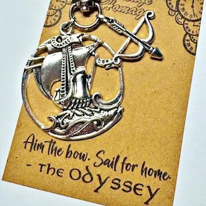 May include: A silver-coloured metal keyring featuring a circular charm with a ship and a bow and arrow. The keyring is attached to a tan display card printed with the text: Aim the bow. Sail for home. - The Odyssey, and Vintage Homage.