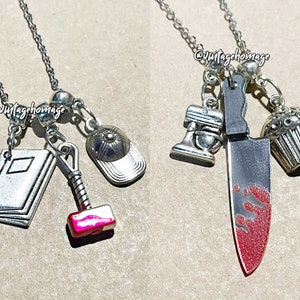 May include: Two silver necklaces with charms. One necklace has a book, a hammer, a baseball cap, and silver beads. The other necklace has a knife with red paint, a cupcake, a mixer, and silver beads. Both necklaces have the text "@vintagehomage" on the beads.
