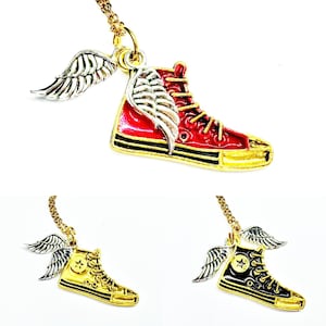May include: Three necklaces featuring high-top sneaker charms with attached silver-toned wings. One charm is red with gold laces, one is solid gold-toned, and one is black with gold laces. Each sneaker pendant hangs from a gold-toned metal chain.