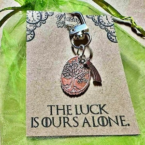May include: A silver keychain with a tree of life pendant and a shooting star charm. The pendant is oval-shaped with a detailed tree design in a copper color. The card reads "THE LUCK IS OURS ALONE."