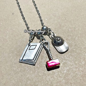 May include: A silver chain necklace with multiple charms, including a book, a hammer, and a baseball cap. The hammer charm has a red accent.