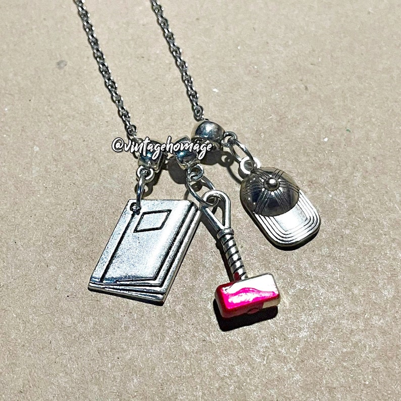 May include: A silver chain necklace with multiple charms, including a book, a hammer, and a baseball cap. The hammer charm has a red accent.