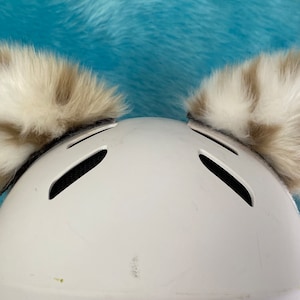 May include: White helmet with two fluffy brown and white faux fur earmuffs attached to the top.
