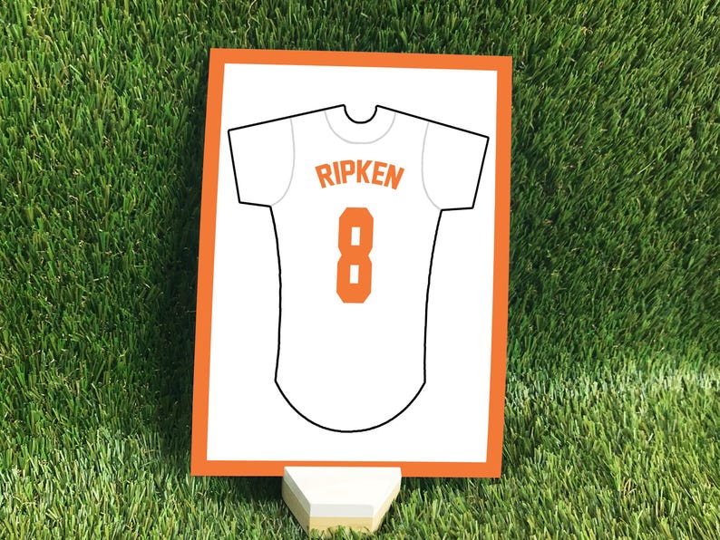 May include: A rectangular sign with an orange border featuring a white baseball jersey graphic. The jersey displays the name RIPKEN in orange letters above the number 8 in orange. The sign is supported by a small, light-colored wooden stand.