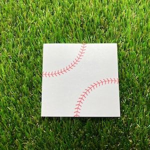 May include: A square white card featuring a graphic print of two curved red baseball stitch patterns. The design mimics the appearance of a baseball with its characteristic red lacing detail set against a plain white background surface.