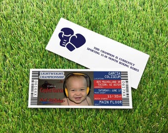 May include: A rectangular ticket-style invitation featuring a photo of a smiling baby wearing yellow headphones, with text reading LIGHTWEIGHT CHAMPIONSHIP, Cayden Garcia, First Birthday, Garcia Coliseum, and 11:30 AM, plus a card with blue boxing gloves.