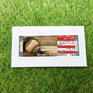 A baseball ticket invitation, over a white envelope over a grass background