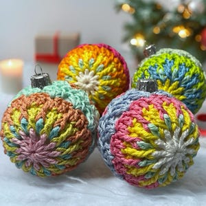 May include: Four spherical Christmas baubles covered in multi-coloured crochet yarn. Each bauble features a radial pattern of stitches in shades of pink, yellow, blue, green, and orange, topped with a silver-toned metal cap for hanging.