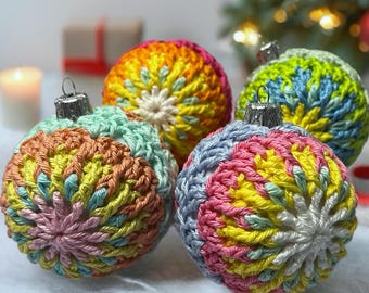 May include: Four spherical Christmas ornaments covered in multi-colored crochet yarn. Each ornament features a radial pattern of stitches in shades of pink, yellow, blue, green, and orange, topped with a silver-toned metal cap for hanging.