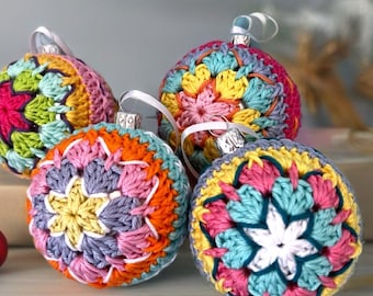 May include: Four spherical Christmas ornaments covered in intricate, multi-colored crochet patterns. Each ornament features a star-like design in shades of pink, yellow, orange, light blue, and white, topped with a silver cap and a white ribbon loop.