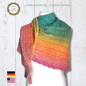 Könnte beinhalten: Ein mehrfarbiger Häkelschal in Rosa-, Orange-, Gelb- und Türkistönen. Der Schal ist über einer Schaufensterpuppe drapiert und weist ein strukturiertes Stichmuster und rosa Quasten auf. Der Text "Häkelanleitung - Crochet Pattern" ist sichtbar.