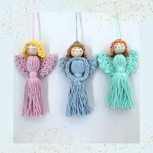 Op de afbeelding: Drie handgemaakte engelenornamenten in pastelkleuren. Elke engel heeft een houten kralen hoofd met garen haar en gehaakte vleugels. De lichamen zijn gemaakt van lange strengen garen in roze, blauw en mintgroen. Elke engel heeft een touwtje om op te hangen.
